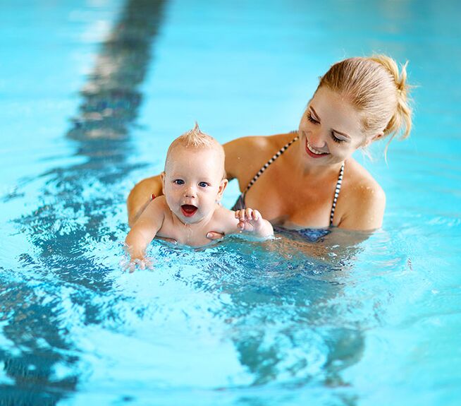 Frau hält lächelndes Baby beim Babyschwimmen.