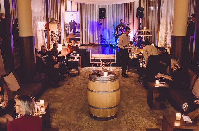 Gyertyafényes lounge a Darwin's bárban, élő gitáros a színpadon, vendégek a kanapékon, pincérek italokat szolgálnak fel.